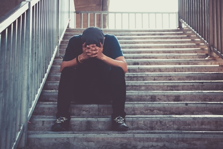 sad man sitting on concrete stairs in a stairway with his head in his hands